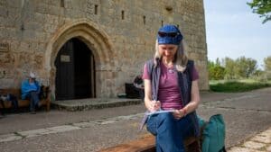 Warum meine Schreibreisen anders sind - Frau sitzt vor einer historischen Kirche und schreibt in ein Buch
